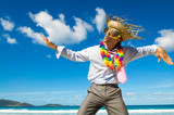 Dancing office worker wearing sunglasses, tourist straw hat and lei celebrating on a tropical beach