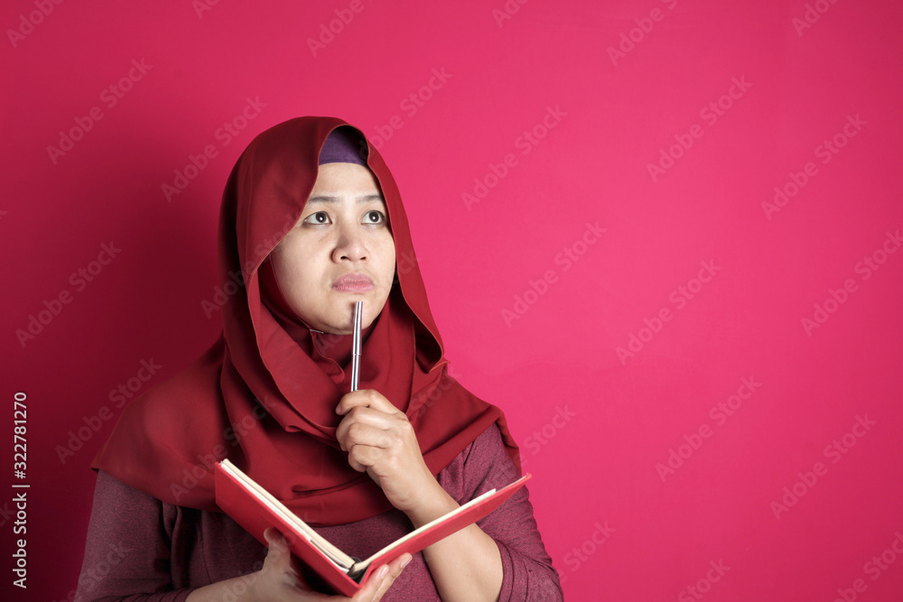 Happy confident successful Asian muslim woman wearing hijab writing on book, smiling and thinking Happy confident successful Asian muslim woman wearing hijab writing on book, smiling and thinking