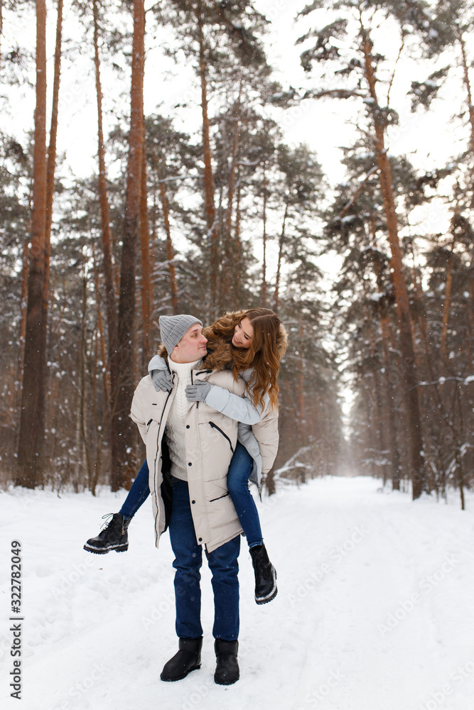 Happy lovers a guy and a girl who love each other hug, kiss, laugh, rage and walk in warm jackets in winter against the background of a snowy forest, a friendly family fun walk Happy lovers a guy and a girl who love each other hug, kiss, laugh, rage and walk in warm jackets in winter against the background of a snowy forest, a friendly family fun walk