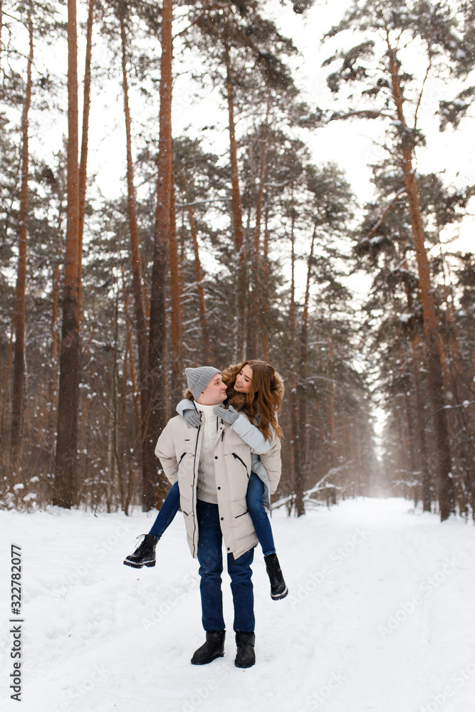 Fototapeta premium Happy lovers a guy and a girl who love each other hug, kiss, laugh, rage and walk in warm jackets in winter against the background of a snowy forest, a friendly family fun walk