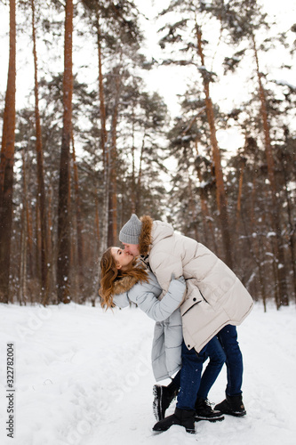 Happy lovers a guy and a girl who love each other hug, kiss, laugh, rage and walk in warm jackets in winter against the background of a snowy forest, a friendly family fun walk