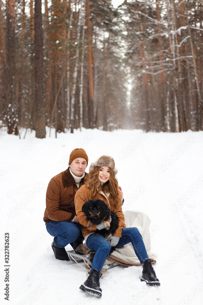 Obraz premium happy couple in love in warm jackets walking with their pet, with a dog, in the snow forest in winter, family trip