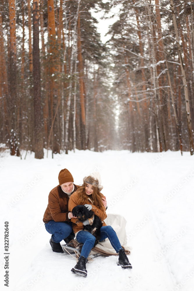 happy couple in love in warm jackets walking with their pet, with a dog, in the snow forest in winter, family trip happy couple in love in warm jackets walking with their pet, with a dog, in the snow forest in winter, family trip