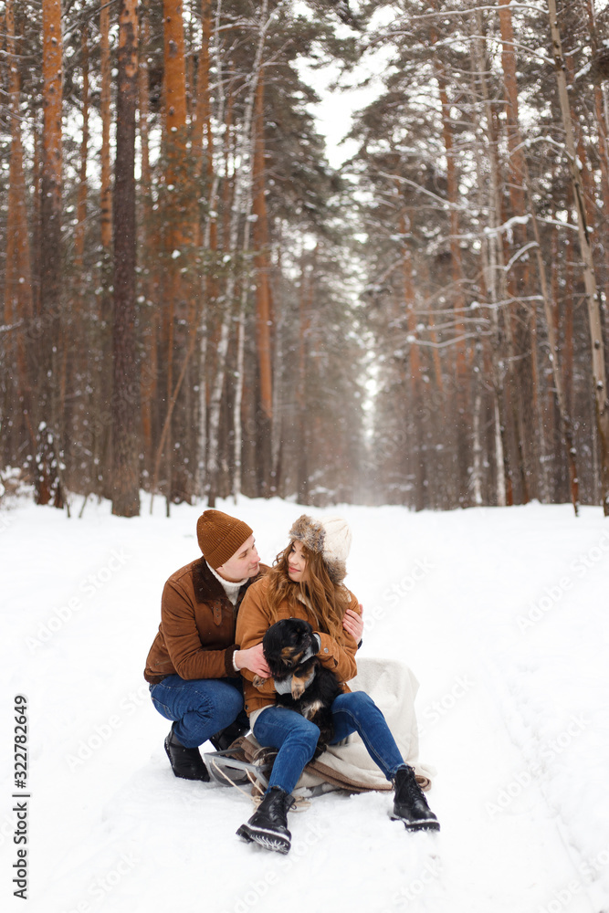 Fototapeta premium happy couple in love in warm jackets walking with their pet, with a dog, in the snow forest in winter, family trip