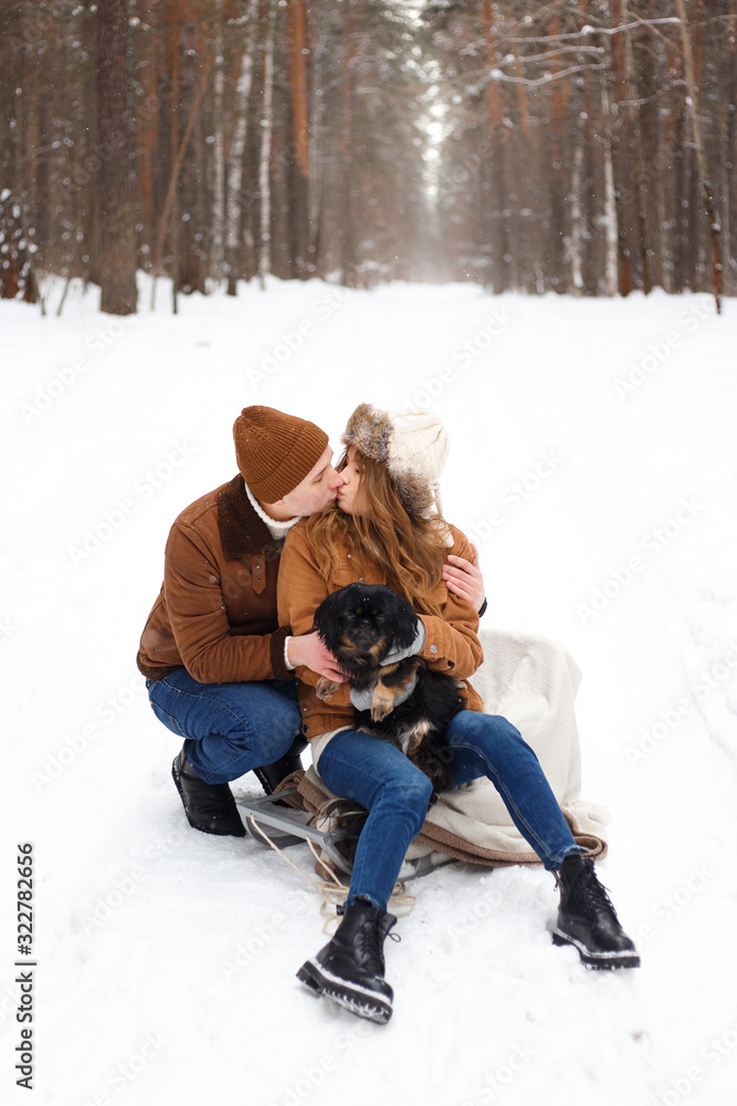 Fototapeta premium happy couple in love in warm jackets walking with their pet, with a dog, in the snow forest in winter, family trip