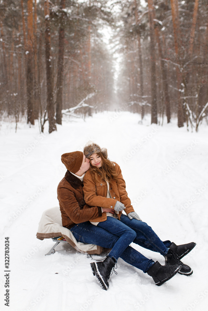 Fototapeta premium Happy lovers a guy and a girl who love each other hug, kiss, laugh, rage and walk in warm jackets in winter against the background of a snowy forest, a friendly family fun walk