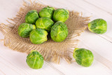 Lot of whole fresh green brussels sprout on natural sackcloth on white wood