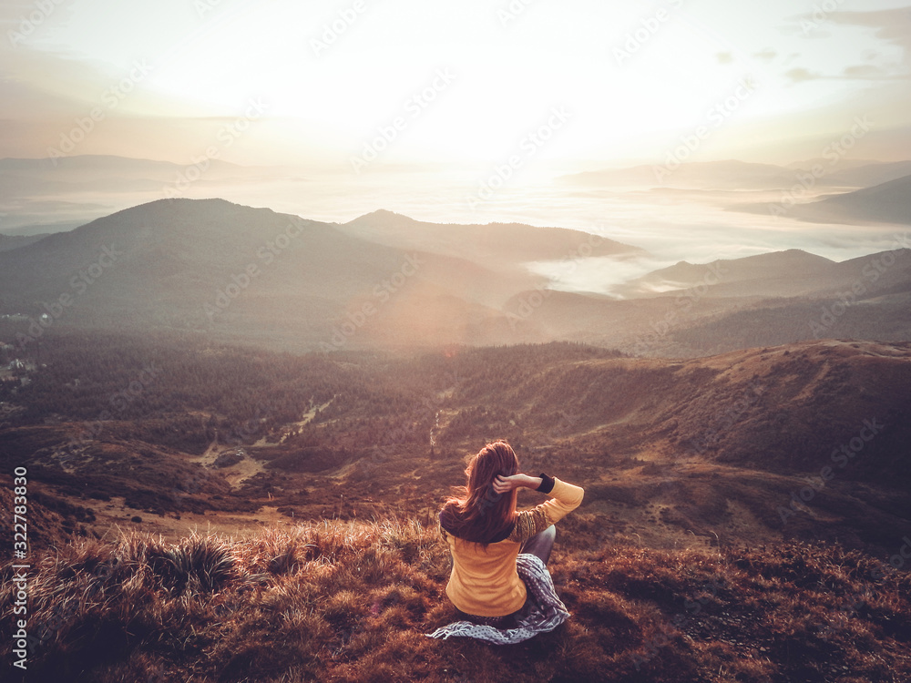 A young brown-haired woman greets the dawn. Enjoys the sunrise. Holds hand over head. Enjoys life and watches watching the sun. Yoga and relaxation high in the mountains. Silhouette of the back view