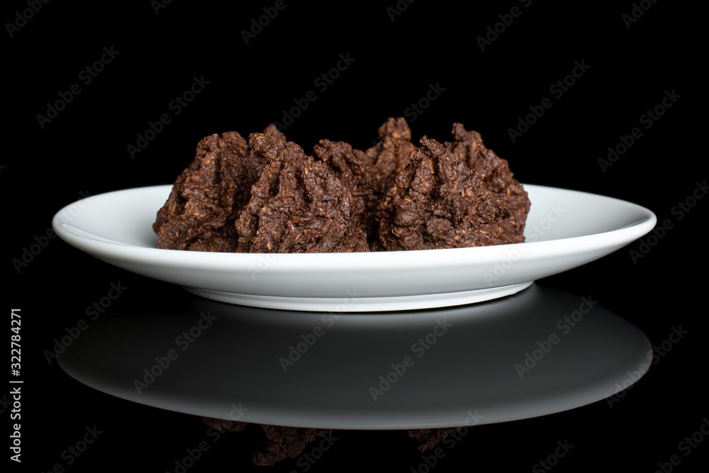Group of four whole homemade brown coconut cocoa biscuit on white ceramic plate isolated on black glass Group of four whole homemade brown coconut cocoa biscuit on white ceramic plate isolated on black glass