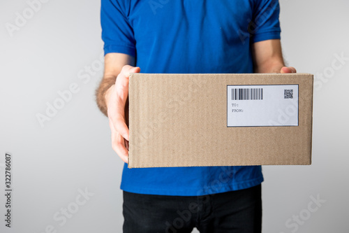 Cropped view of courier holding cardboard box with barcode and qr code isolated on grey