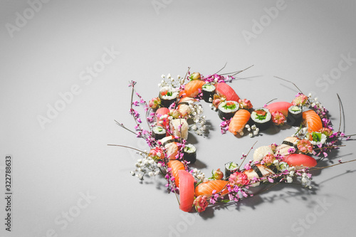 Heart made of sushi and flowers. Love sushi. Valentines Day (14 February), Mother's day, Woman's day (8 March) or spring concept. Creative romantic. Japanese sushi set on gray background. Copy space