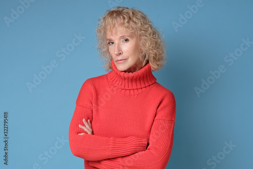 Elderly lady with a lively smile looking directly at the camera while posing against a blue background