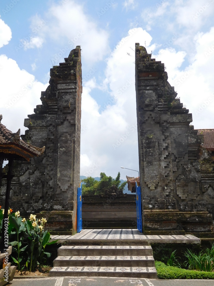 Ulun Danu Beratan Temple, Bali temple gate, carved large stone gate with steps leading up and sunny blue sky background Ulun Danu Beratan Temple, Bali temple gate, carved large stone gate with steps leading up and sunny blue sky background