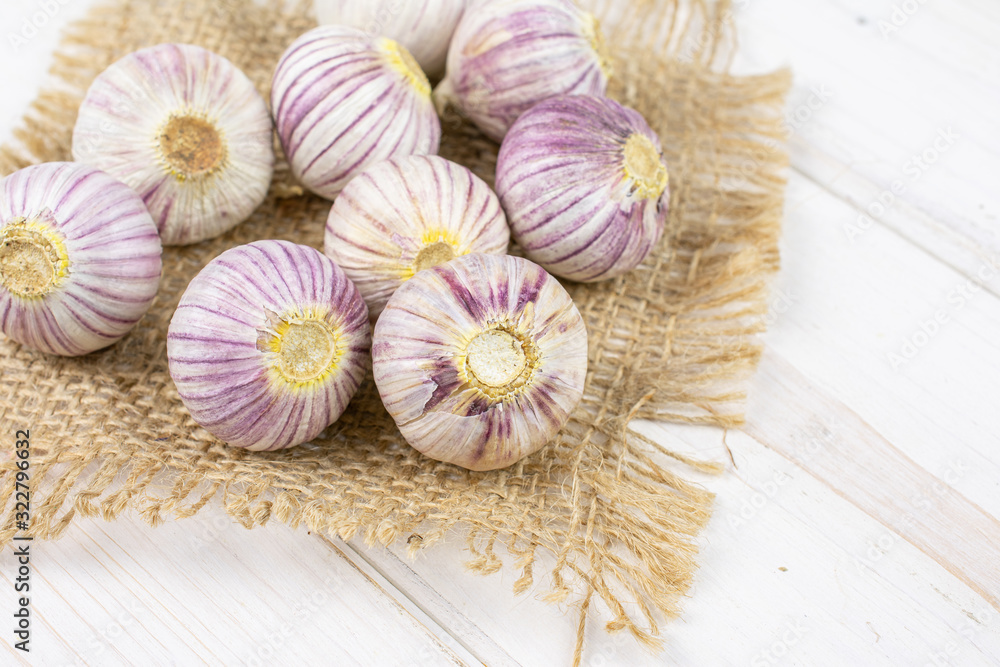 Lot of whole fresh purple single clove garlic on natural sackcloth on white wood Lot of whole fresh purple single clove garlic on natural sackcloth on white wood
