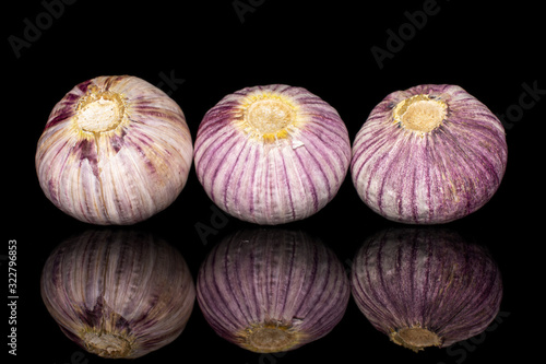 Group of three whole fresh purple single clove garlic in row isolated on black glass