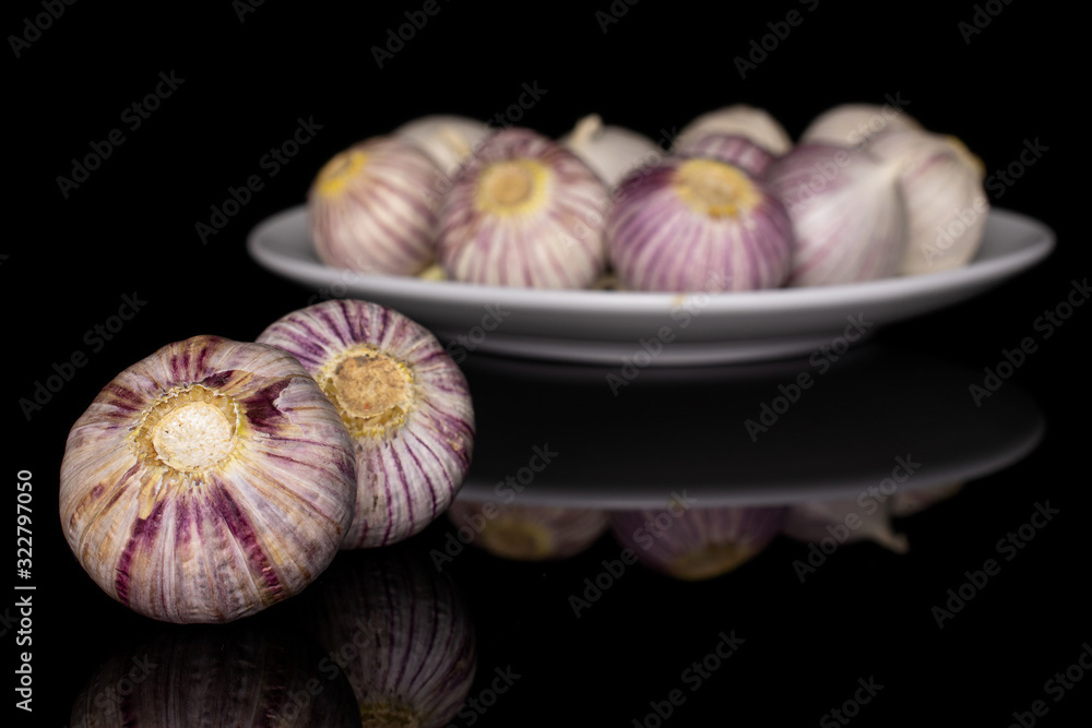 Lot of whole fresh purple single clove garlic on white ceramic plate isolated on black glass Lot of whole fresh purple single clove garlic on white ceramic plate isolated on black glass