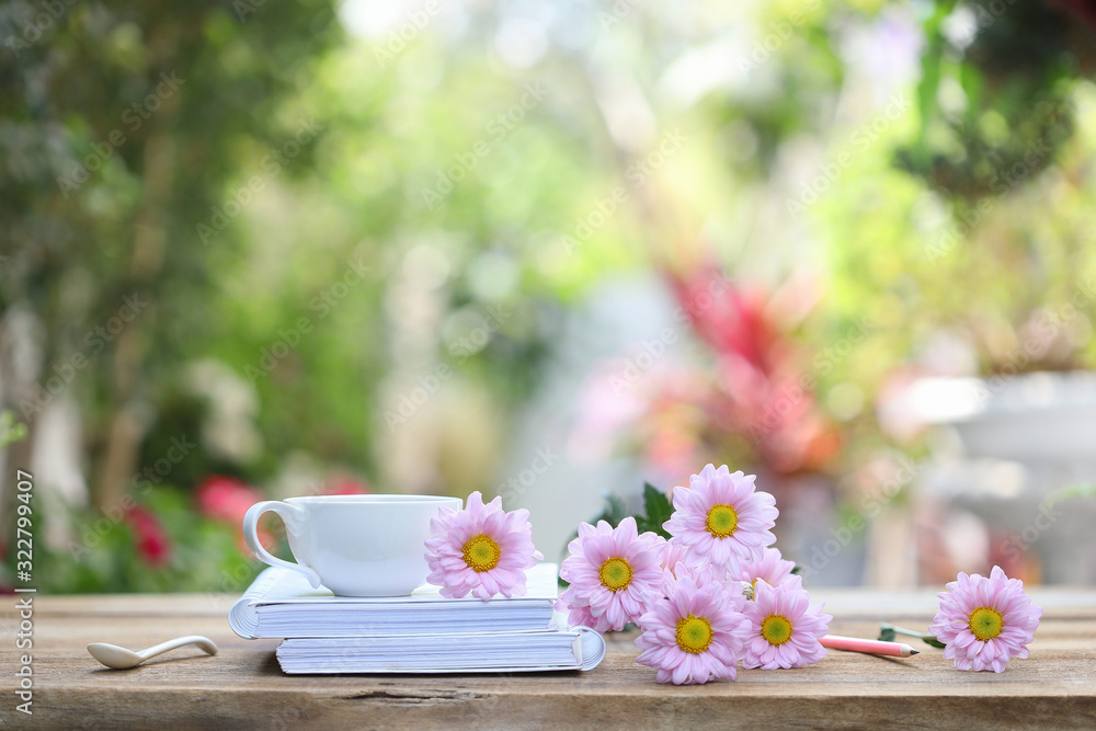 White coffee cup with white notebook and pink pencil with pink Chrysanthemum flower on wooden table at outdoor 