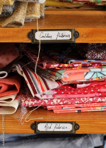A wooden shelf of red fabric, a brass plate labels the colours , a textile storage unit 