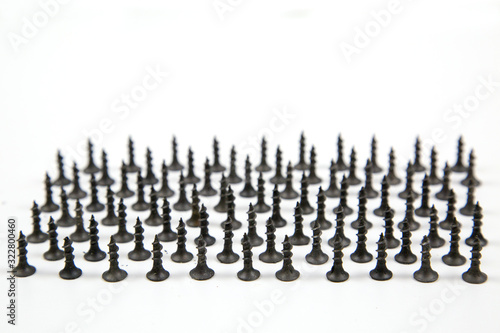 Small black wood screws (bedbugs) lined up in rows, isolated on a white background, the idea is the concept of free space for text. Construction, repair, fasteners.