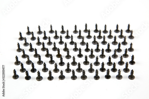 Small black wood screws (bedbugs) lined up in rows, isolated on a white background, the idea is the concept of free space for text. Construction, repair, fasteners.