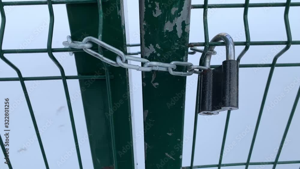 A green lattice door closed on a chain with a barn lock is trying to open. The Winter. Grimly. A green lattice door closed on a chain with a barn lock is trying to open. The Winter. Grimly.