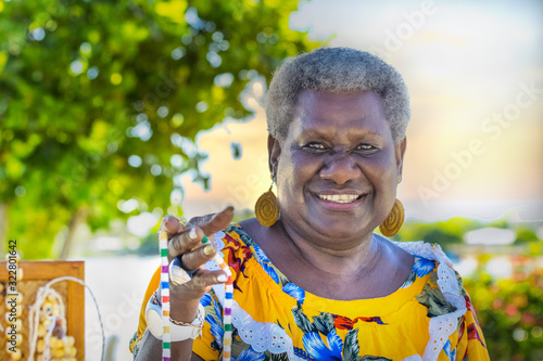 Portrait of a melanesian - australian mature woman smiling, showing the hand-made jewerly that she has made, outdoors. photo