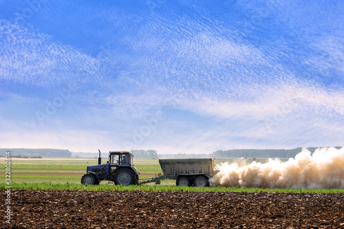 tractor pulling a trailer spraying fertilizer in a cloud of dust
