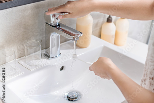 Dental care. Woman hands is holding toothbrush with toothpaste in bathroom, sink and running faucet in background"
