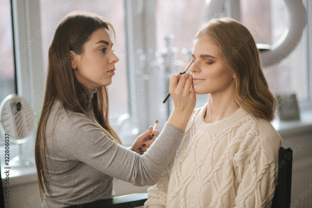 Makeup artist work in her beauty studio. Portrait of Woman applying by professional make up master. Beautiful make up artist start making a makeup for blond hair model Makeup artist work in her beauty studio. Portrait of Woman applying by professional make up master. Beautiful make up artist start making a makeup for blond hair model