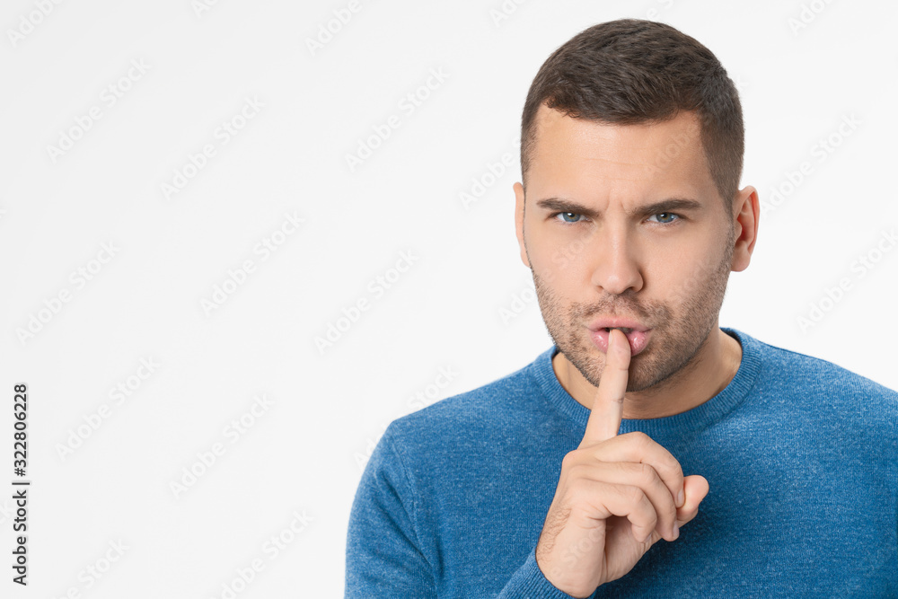 Close up of young man showing silence gesture standing isolated over white background Close up of young man showing silence gesture standing isolated over white background