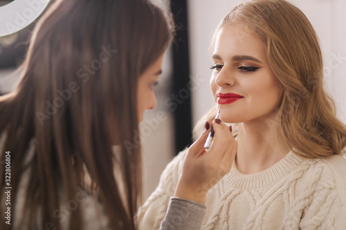 Makeup artist work in beauty studio. Woman applying by professional make up master. Beautiful make up artist make a makeup for blond hair model