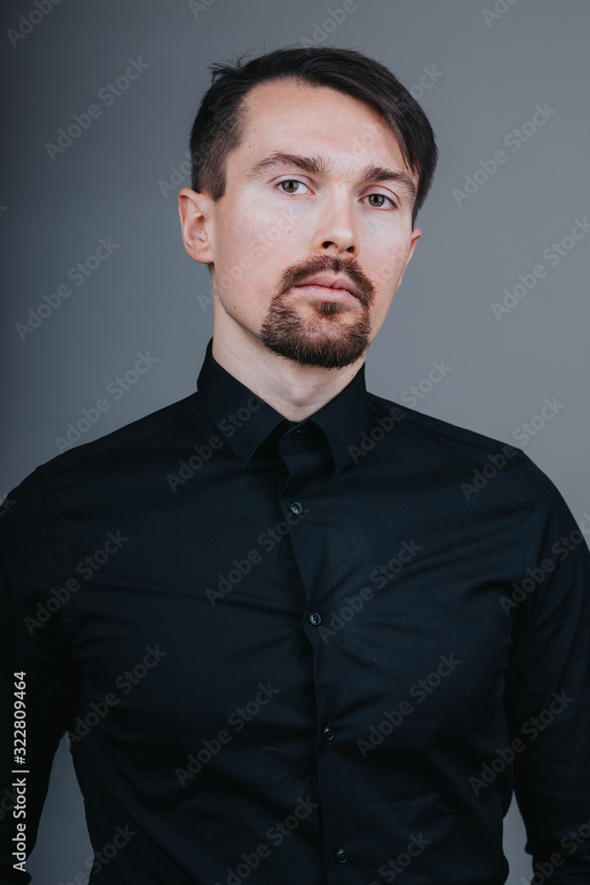 Photo of a handsome man with a coolly stylized scrub and hairstyle. Photo taken in a photo studio on a gray background. The man tries to express his emotions with gesticulation and mimics.