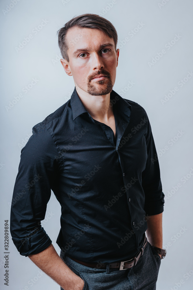 Photo of a handsome man with a coolly stylized scrub and hairstyle. Photo taken in a photo studio on a gray background. The man tries to express his emotions with gesticulation and mimics. Photo of a handsome man with a coolly stylized scrub and hairstyle. Photo taken in a photo studio on a gray background. The man tries to express his emotions with gesticulation and mimics.