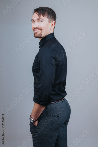 Photo of a handsome man with a coolly stylized scrub and hairstyle. Photo taken in a photo studio on a gray background. The man tries to express his emotions with gesticulation and mimics. © kamil
