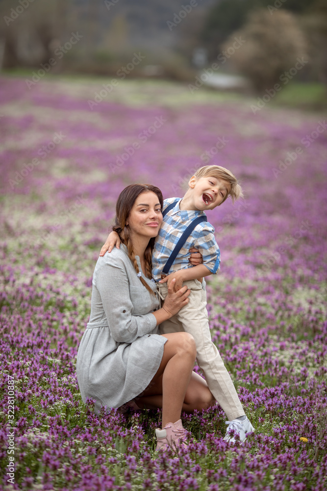 Fototapeta premium Mom tickles son. A family of two a mother and son of a child walk through a young lavender field