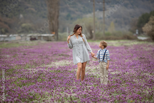Beautiful mom holds her son's hand on a walk. A family of two a mother and son of a child walk through a young lavender field