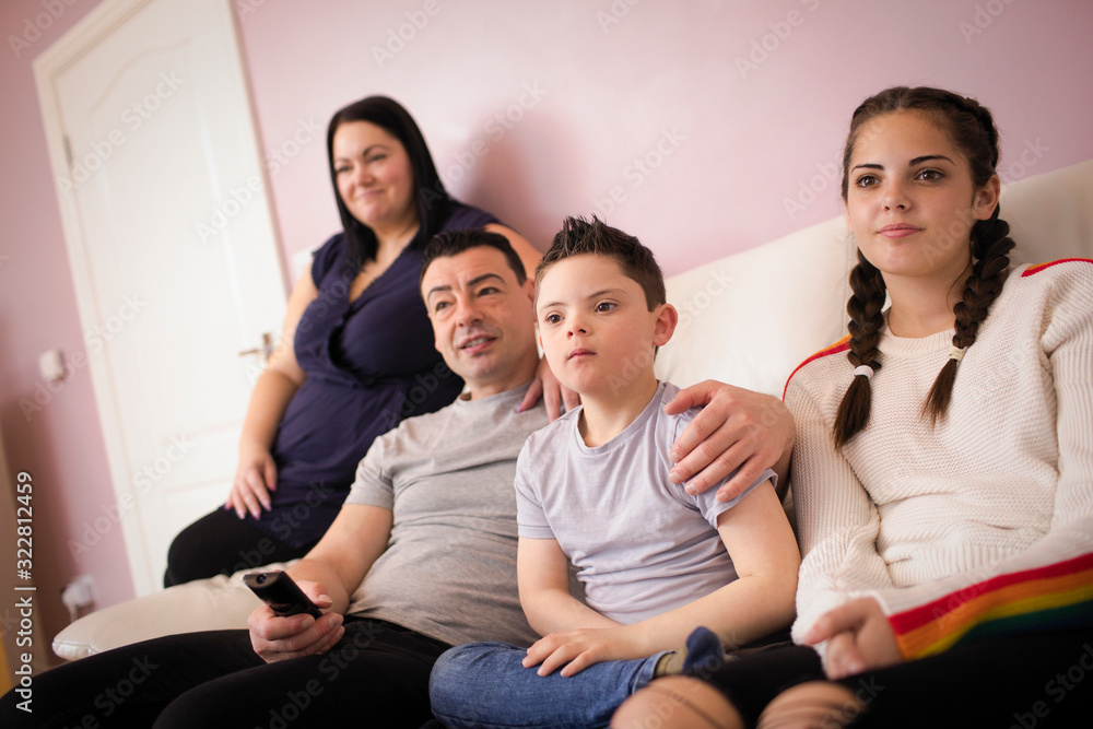 Family with Down Syndrome son watching TV on living room sofa Family with Down Syndrome son watching TV on living room sofa
