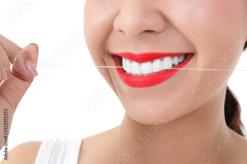A beautiful young woman wearing red lip with beautiful arranged teeth. She is using dental floss to clean all the food particles that are stuck in the spaces of her teeth. Oral care concepts