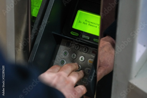 ATM or credit paying terminal with green display showing "Processing do not remove card" text, detail on man hand over steel keypad