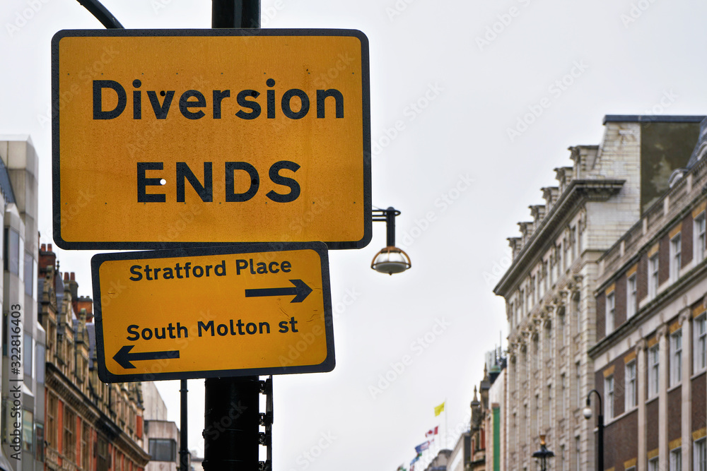 Yellow and black Diversion Ends sign with arrows pointing to Stratford Place and South Molton street, blurred building in background Yellow and black Diversion Ends sign with arrows pointing to Stratford Place and South Molton street, blurred building in background