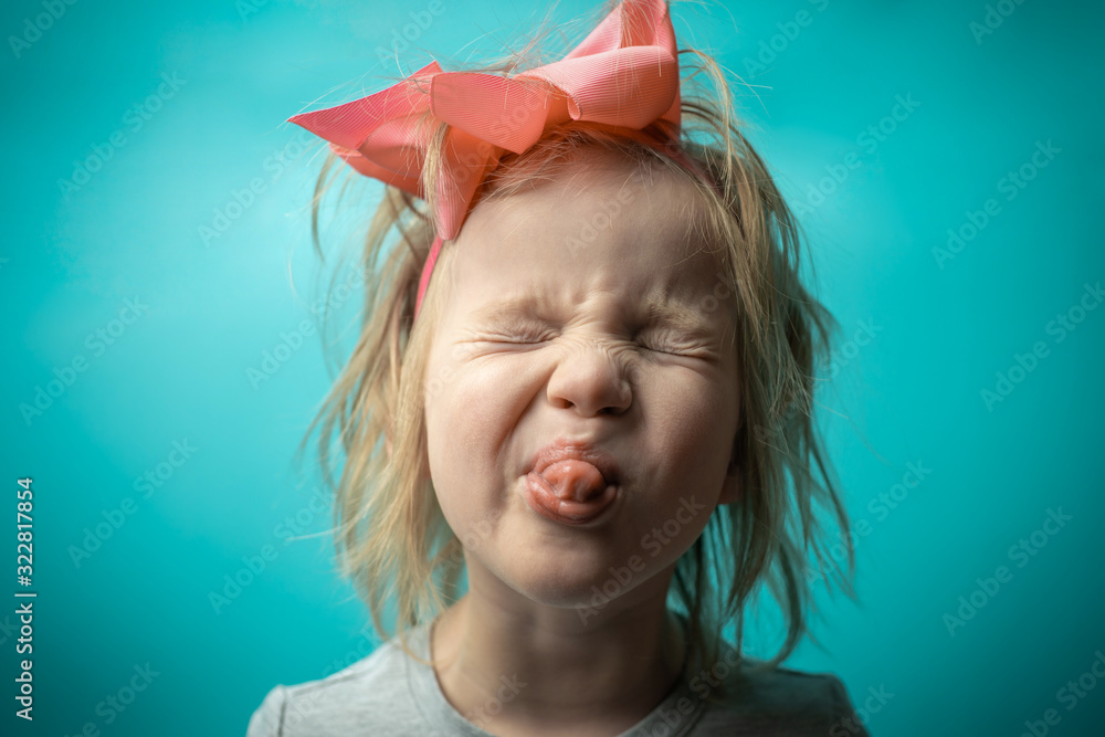 girl is mischievous. rebellious child. little girl with a pink bow on a blue background. girl shows his tongue girl is mischievous. rebellious child. little girl with a pink bow on a blue background. girl shows his tongue