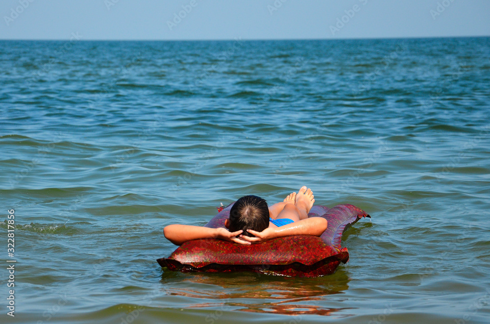 A teenager lies on an air mattress in the sea and enjoys the peace.