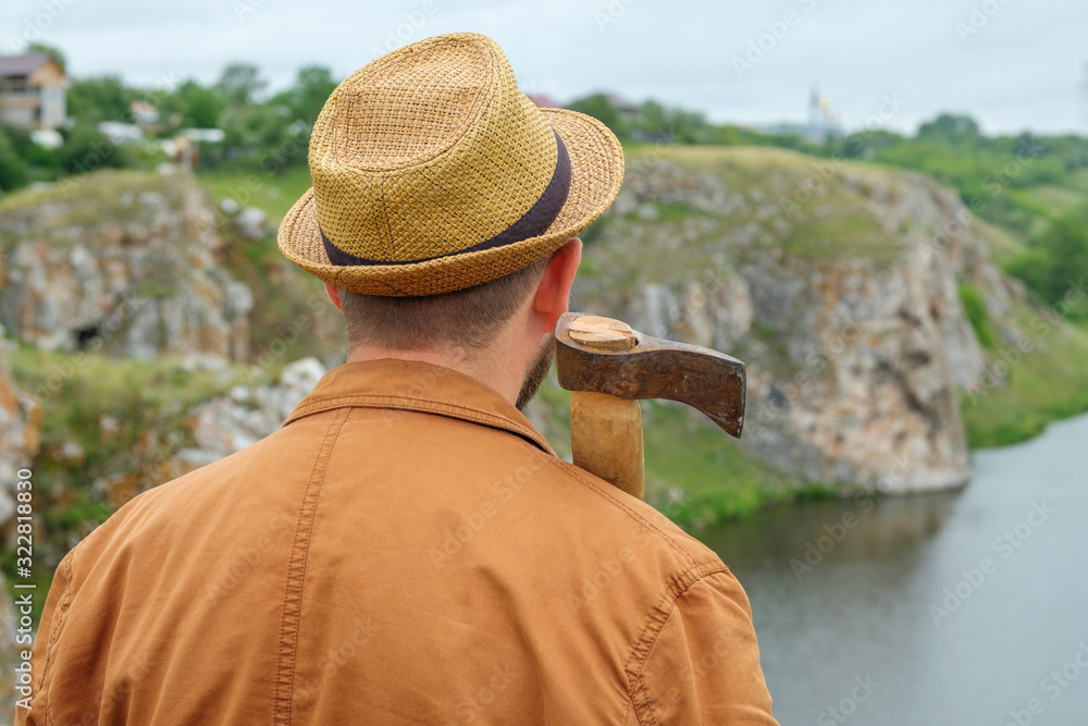 a man in a hat looks at the landscape of the river and rocks on the shoulder of an axe