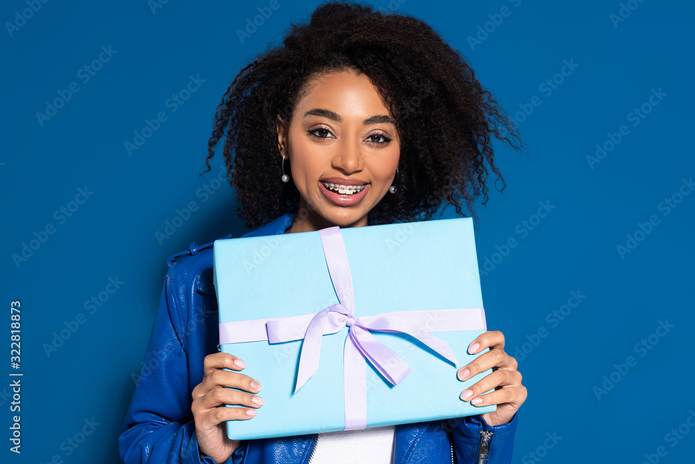 smiling african american woman holding present on blue background smiling african american woman holding present on blue background