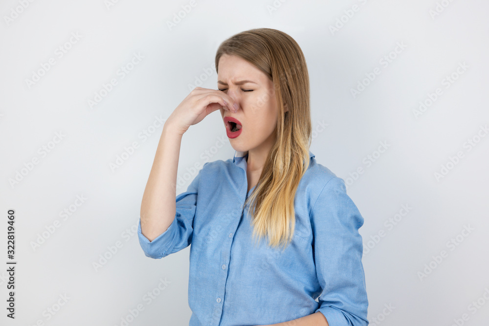 young blond woman closing her nose from bad smell standing on isolated white background, body language young blond woman closing her nose from bad smell standing on isolated white background, body language