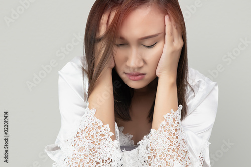  Asian woman in lace nightgown and white satin robes has a headache, isolated on gray background. Suffering migraine. photo