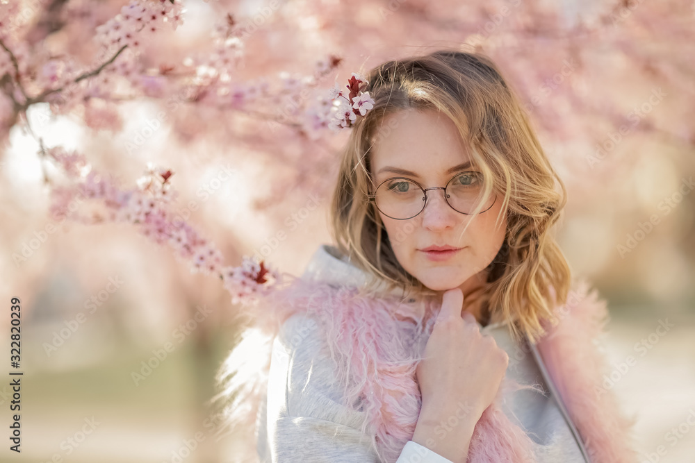 Portrait of a blonde woman against a backdrop of pink flowers. Portrait of female model near pink peach blossom tree