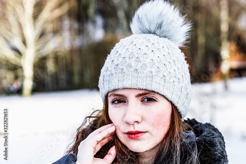 A girl in a hat with a slight smile on the background of a winter forest