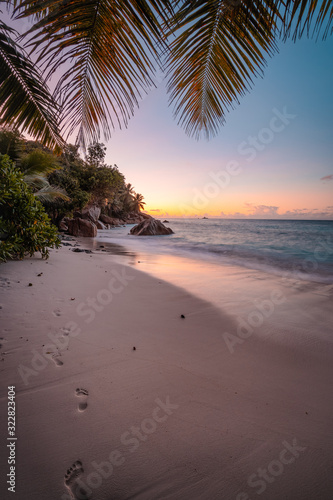 La Digue Island, Seychelles. Beautiful sunset lit colorful sky on exotic tropical sandy beach with foot prints