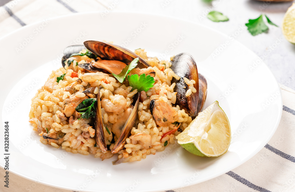 Seafood risotto in a white plate on the served table. Risotto with shrimp, tomatoes, parsley and mussels in shells. Tasty and healthy Mediterranean cuisine. Seafood risotto in a white plate on the served table. Risotto with shrimp, tomatoes, parsley and mussels in shells. Tasty and healthy Mediterranean cuisine.